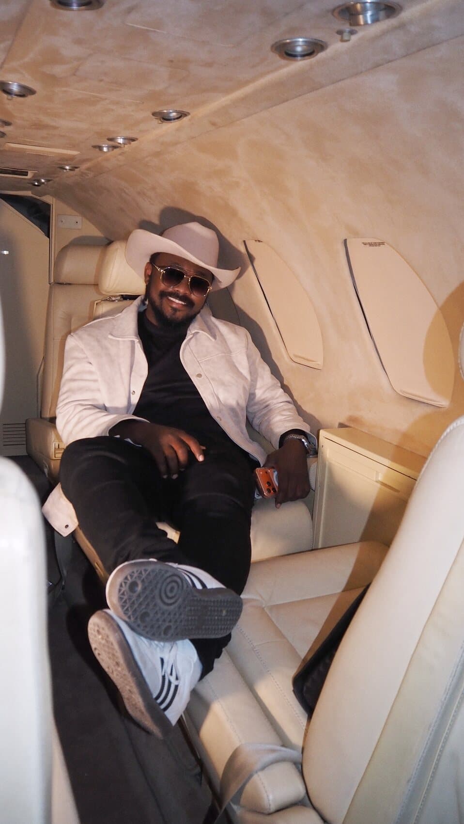 ABJKOREA reclining in the cabin of a private jet in a pale cowboy hat and sunglasses.