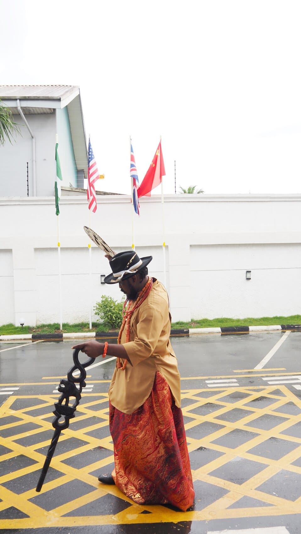 ABJKOREA in traditional regalia before the flags of Nigeria, the USA, the UK and China.