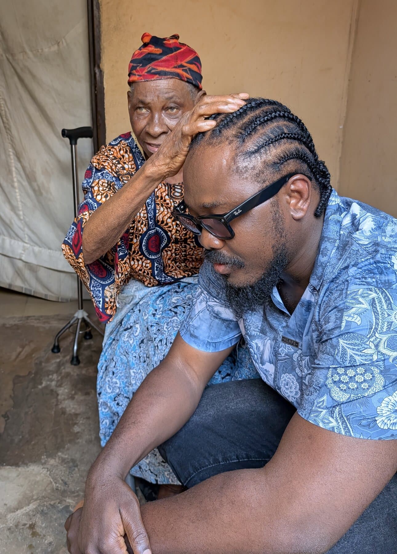 An elder tenderly rests her hand on ABJKOREA's head — a quiet moment of blessing and belonging.